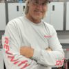 A person with long hair is smiling and standing with arms crossed, wearing a black baseball cap that says "Team Revvvify" and dressed in a light gray Long Sleeve T-Shirt featuring the "Team Revvvify" logo in red on both the front and sleeves.