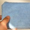 A hand is holding a rectangular, blue Microfiber Sponge against a neutral background. The textured surface of the sponge highlights the typical microfiber material characteristics, making it as versatile as any traditional sponge for cleaning tasks.