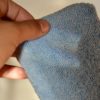 A hand holding a Microfiber Sponge close up. The sponge, with its textured surface, gleams softly under the light, highlighting the intricate fibers. The background is softly blurred, enhancing the focus on the microfiber's detail.