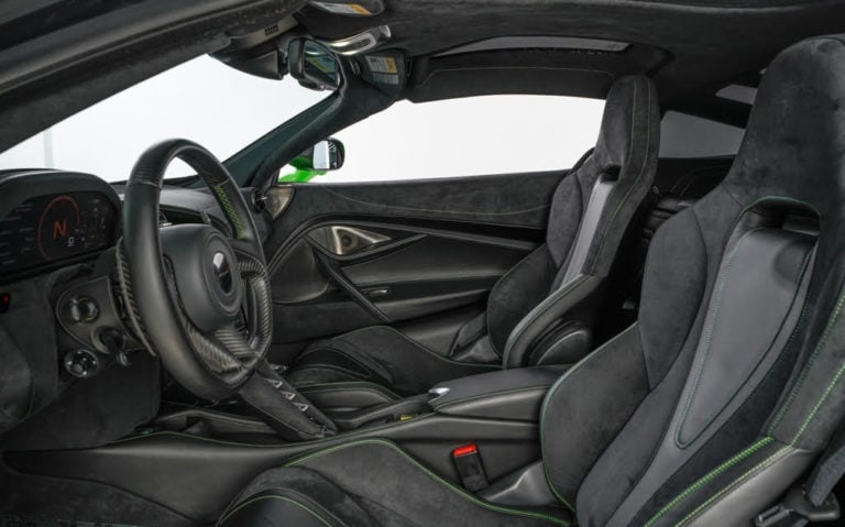 The interior of a luxury sports car featuring black suede and leather seats with green accents, a carbon fiber console, and a sleek steering wheel. The design showcases high-end materials and meticulous craftsmanship for an upscale, sporty look.