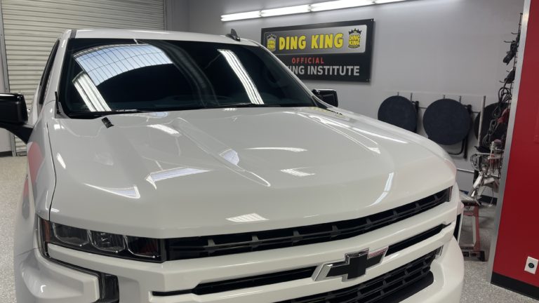 A white Chevrolet pickup truck is parked indoors at the Official Ding King PDR Training Institute. The truck is in a clean workshop area with equipment and tools visible in the background. The Ding King sign is displayed on the wall behind the truck.