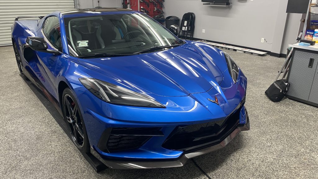 A blue sports car with sleek, aerodynamic design is parked in a clean, organized garage. The vehicle has a low profile, sharp angles, and prominent headlights. Various tools and garage equipment are visible in the background.