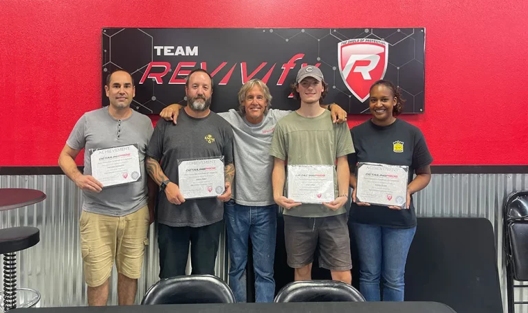 Five people stand in a row holding certificates in a room with a red wall and a "Team Revivif" sign behind them. The group includes three men and two women, all smiling at the camera.