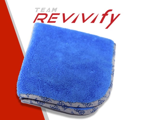 A blue microfiber towel is neatly folded with a partial view of its patterned backing. The background features a white and red design with the text "TEAM REVIVIFY" in grey and red letters.