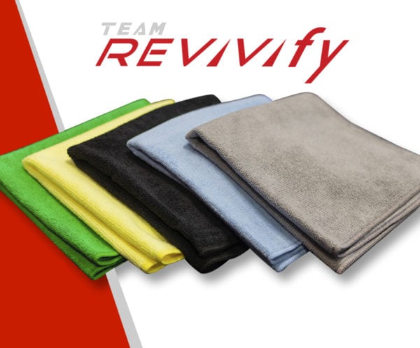 A variety of colored Revivify Microfiber Towels, including green, yellow, black, blue, and gray, are neatly stacked. The text "TEAM REVIVIFY" is displayed above the towels in a modern, italicized font. The background features a striking red and white diagonal color scheme.